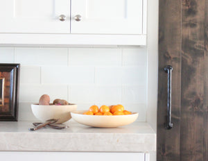 Two bowls with fruit and sugar palm wood salad tongs laying next to them